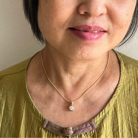 Woman wearing a gold necklace with a pendant against a neutral background