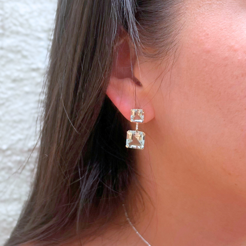 Close-up of a person wearing square-shaped earrings with a neutral background