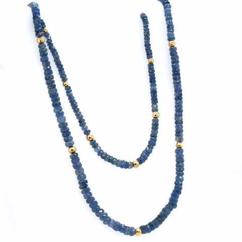 Natural sapphire gemstone strand with gold rondels laid out on neutral surface