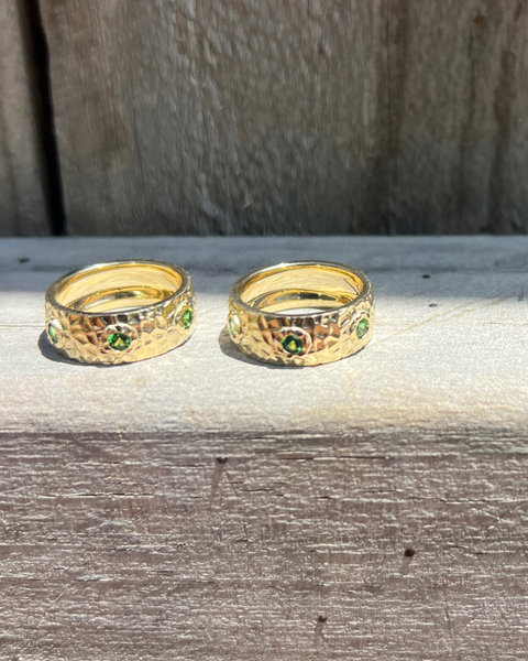 Two gold rings with green gemstones on a wooden surface