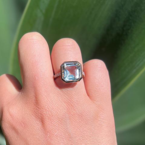 Ring with a large emerald-cut gemstone on a finger against a green leaf background