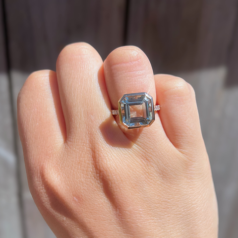 Hand wearing a ring with a large gemstone on a neutral background