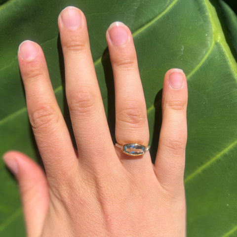 Blue topaz diamond ring worn on hand with a green leaf background